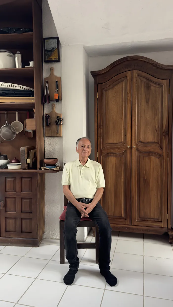Carlos sentado frente al armario de madera, en la sala de la casa.