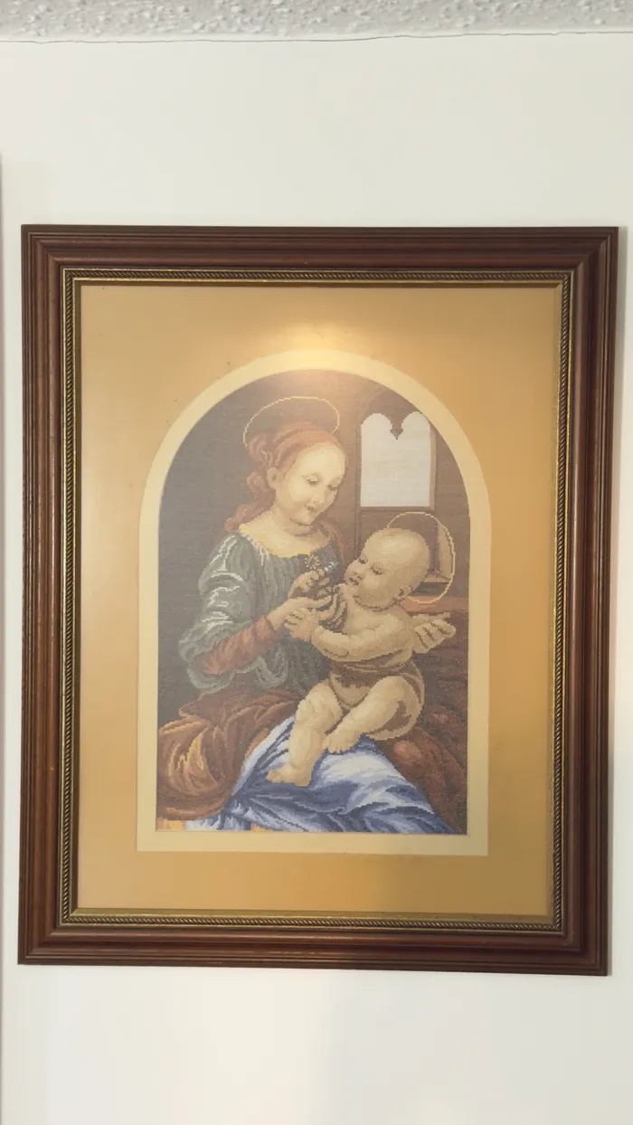 Un bordado de la Virgen con el Niño, enmarcado en madera oscura, colgado en la pared.